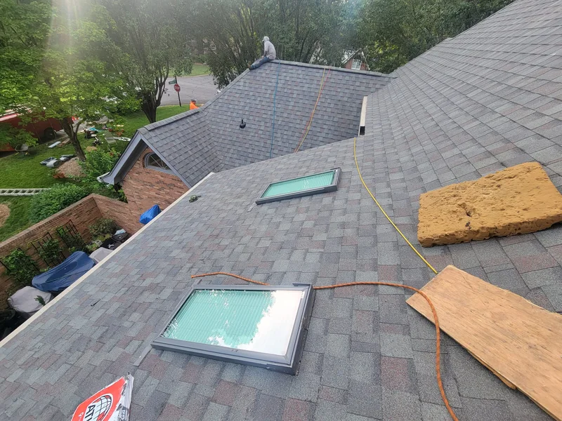 Roofing work in progress around skylights on a gray shingle roof